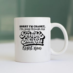 May include: White ceramic coffee mug with black text that reads "Sorry I'm cranky, I'm going through my Terrible Thirties right now".