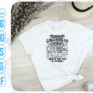 May include: A white t-shirt with a black graphic design that says "Homemade Gingerbread Cookies" and includes a recipe for gingerbread cookies. The recipe includes ingredients like molasses, brown sugar, softened butter, eggs, flour, salt, baking soda, cloves, cinnamon, and ginger. The graphic also includes instructions to bake at 350 degrees Fahrenheit for 8-10 minutes.