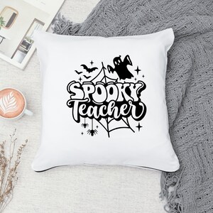 Pu&ograve; includere: Cuscino bianco con testo nero che recita "Spooky Teacher" con un fantasma, pipistrelli, ragni e una ragnatela.