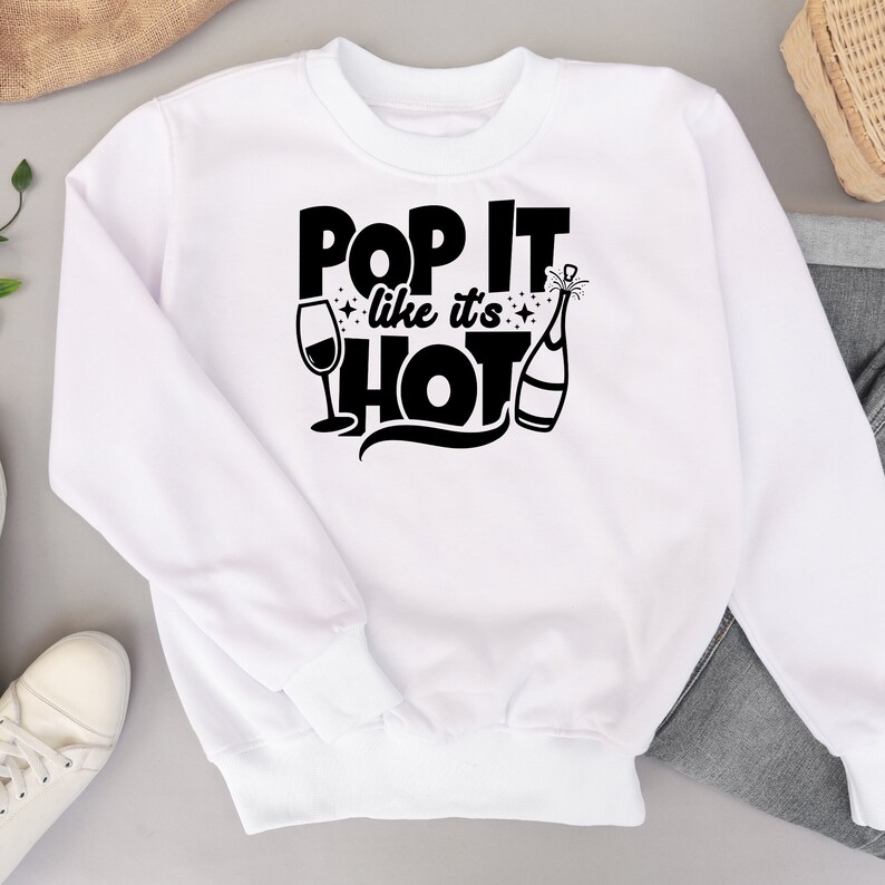 May include: White sweatshirt with black text that reads "Pop It Like It's Hot" with a champagne bottle and glass graphic.