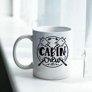 May include: White ceramic mug with a black design of two crossed sticks with marshmallows on the ends. The design also includes a circle with the text "CABIN CREW" inside.