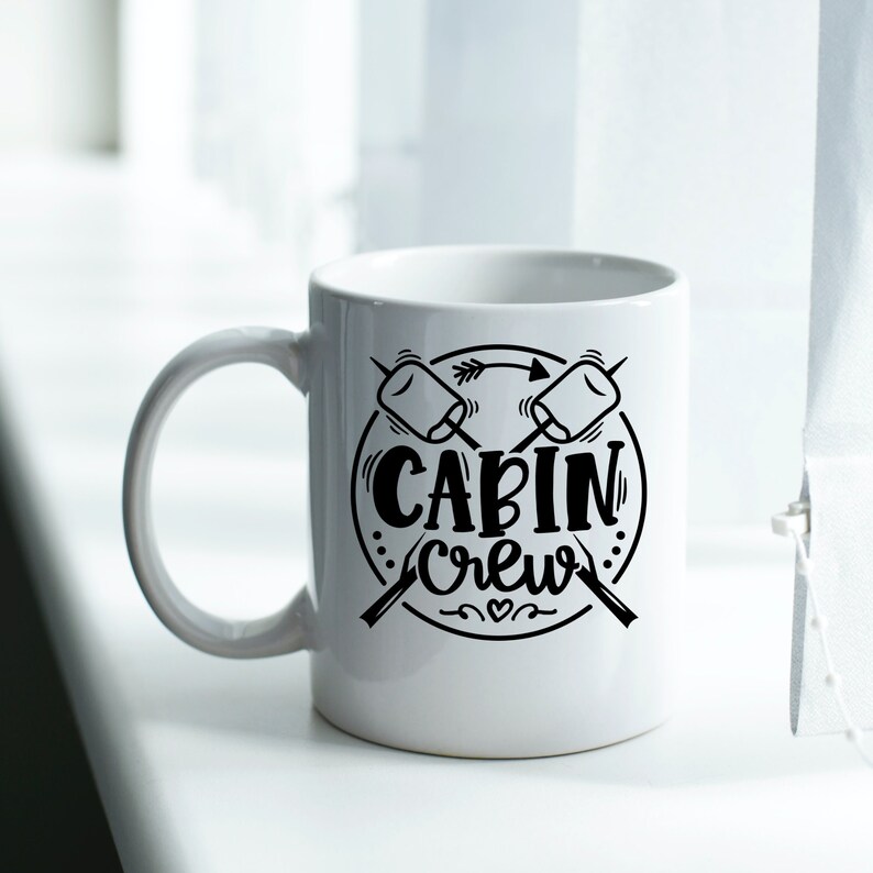 May include: White ceramic mug with a black design of two crossed sticks with marshmallows on the ends. The design also includes a circle with the text "CABIN CREW" inside.