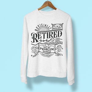 May include: White sweatshirt with black text that reads "Officially Retired" with a decorative design around the text. The text also includes "I'm outta here!" and "Not my problem anymore. Good riddance."