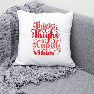 May include: White throw pillow with red text that reads "Thick Thighs Cupid Vibes" with small red hearts surrounding the text.