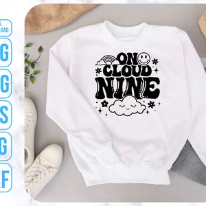 May include: White sweatshirt with black text that reads "On Cloud Nine" with a rainbow, a cloud with eyes, and a smiley face.