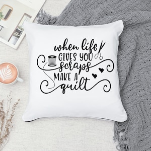 May include: White throw pillow with black text that reads "When life gives you scraps make a quilt". The text is surrounded by decorative swirls and hearts.