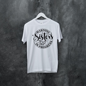 Puede incluir: Camiseta blanca con un gr&aacute;fico circular negro que dice "Warning Sisters Trip in Progress".