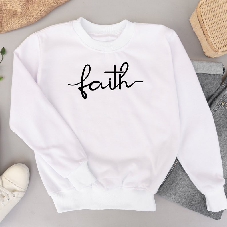 May include: White sweatshirt with the word "faith" written in black cursive script.
