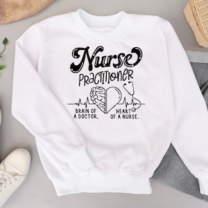 May include: White sweatshirt with black text that reads "Nurse Practitioner" with a brain and heart graphic and the text "Brain of a Doctor, Heart of a Nurse."