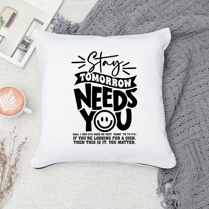 May include: White throw pillow with black text that reads "Stay Tomorrow Needs You" with a smiley face in the "You". The text below reads "Call 1-800-273-8255 or text "HOME" to 741741. If you're looking for a sign, then this is it. You matter."