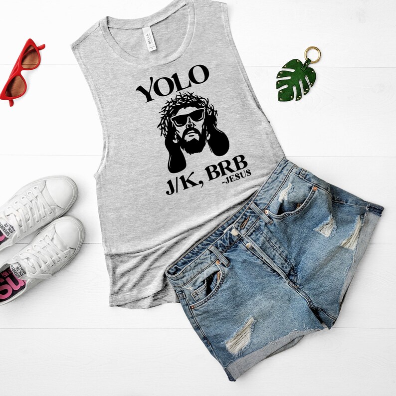 May include: A gray sleeveless muscle tank top with a black graphic of Jesus wearing sunglasses and a crown of thorns. The text "YOLO J/K, BRB -JESUS" is printed on the shirt.