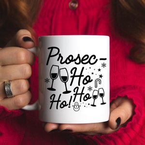 May include: White ceramic mug with a black design that says "Prosec-Ho Ho! Ho!" with a snowman and snowflakes. There are also images of wine glasses.