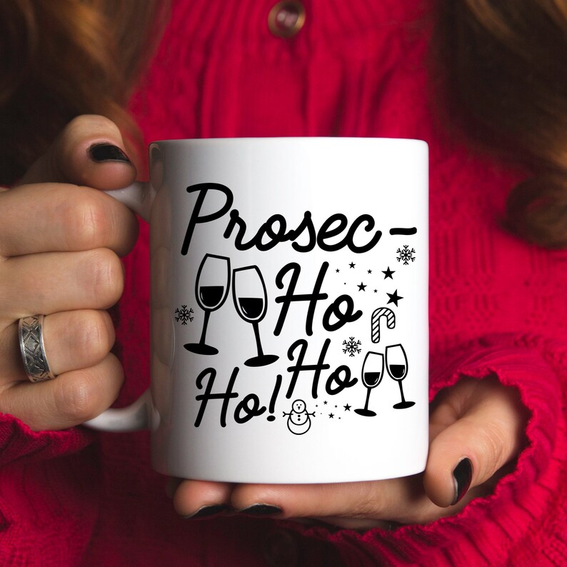 May include: White ceramic mug with a black design that says "Prosec-Ho Ho! Ho!" with a snowman and snowflakes. There are also images of wine glasses.