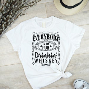 May include: White t-shirt with a black graphic that says "Everybody in da pub drinkin' whiskey".