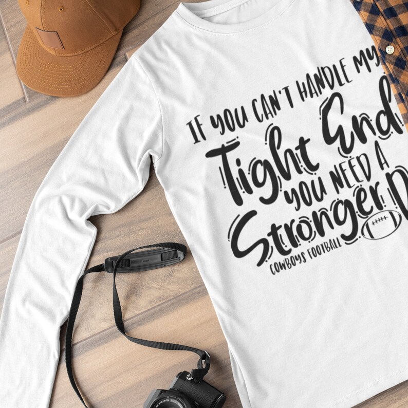 May include: White long-sleeve t-shirt with black text that reads "If you can't handle my tight end you need a stronger D."  The text is in a stylized font and includes a football graphic.  The text "Cowboys Football" is also included.
