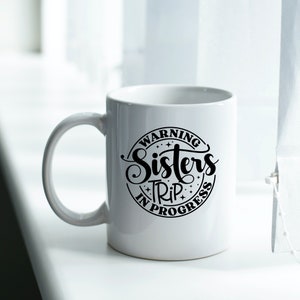 Puede incluir: Taza de caf&eacute; de cer&aacute;mica blanca con un dise&ntilde;o circular negro que dice "Warning Sisters Trip In Progress".