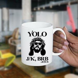 May include: White ceramic mug with a black and white image of Jesus wearing sunglasses and a crown of thorns. The text "YOLO J/K, BRB -JESUS" is printed on the mug.