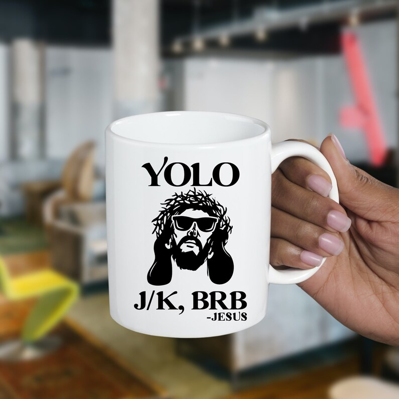 May include: White ceramic mug with a black and white image of Jesus wearing sunglasses and a crown of thorns. The text "YOLO J/K, BRB -JESUS" is printed on the mug.