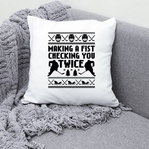 Puede incluir: Coj&iacute;n blanco con un dise&ntilde;o de hockey en blanco y negro. El texto en el coj&iacute;n dice "Making a fist checking you twice".
