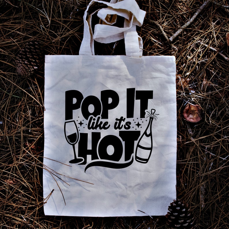 May include: A white canvas tote bag with black text that reads "Pop It Like It's Hot" with a wine glass and champagne bottle graphic.