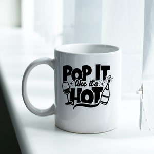 May include: White ceramic mug with a black design that says "Pop It Like It's Hot" with a champagne bottle and a wine glass graphic.