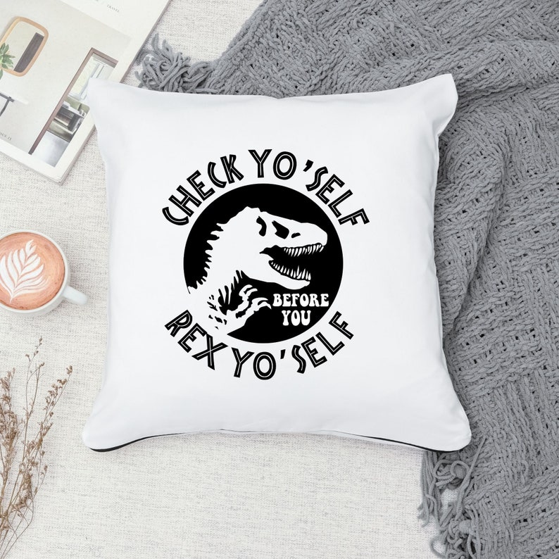 May include: White throw pillow with black text that reads "Check Yo'Self Before Rex Yo'Self" with a black silhouette of a dinosaur inside a circle.