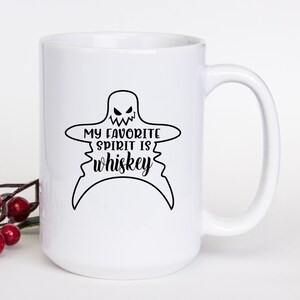 K&ouml;nnte beinhalten: Eine wei&szlig;e Keramik-Kaffeetasse mit einer schwarzen Geistergrafik und dem Text "My favorite spirit is whiskey".