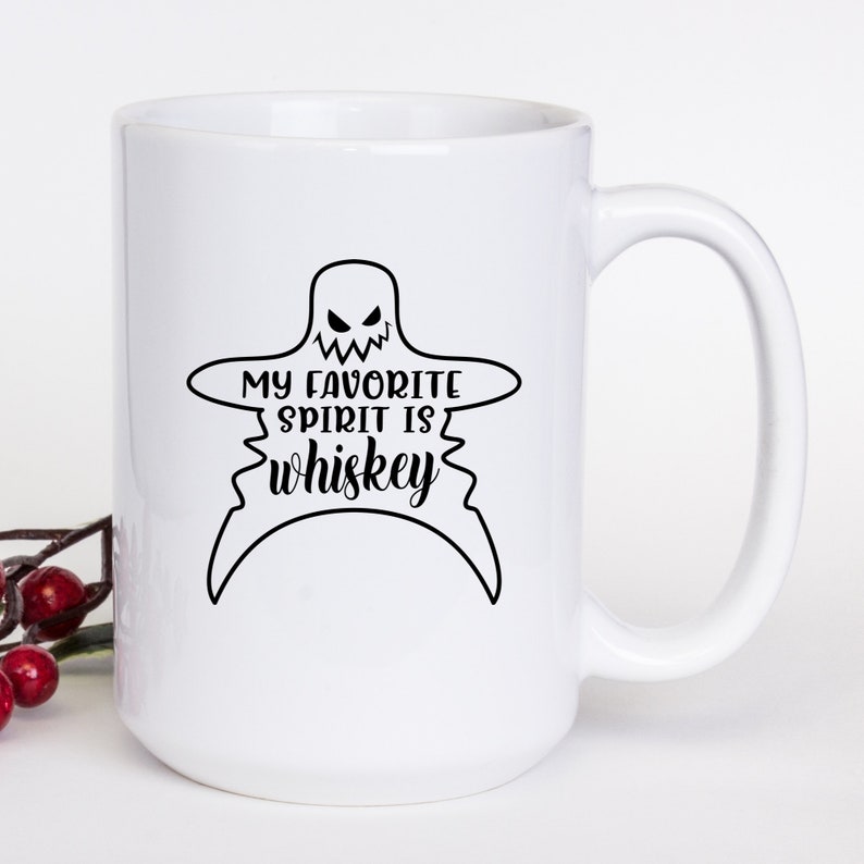 K&ouml;nnte beinhalten: Eine wei&szlig;e Keramik-Kaffeetasse mit einer schwarzen Geistergrafik und dem Text "My favorite spirit is whiskey".