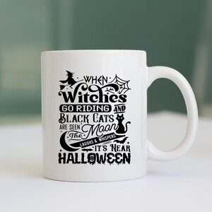 K&ouml;nnte beinhalten: Eine wei&szlig;e Keramik-Kaffeetasse mit einem schwarzen Design, auf dem steht "When Witches Go Riding and Black Cats Are Seen The Moon Laughs & Whispers It's Near Halloween".
