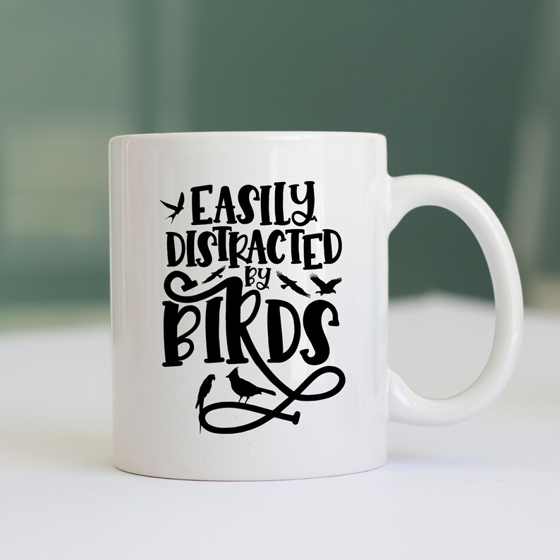 Puede incluir: Taza de cer&aacute;mica blanca con un dise&ntilde;o negro que dice "Easily Distracted by Birds" con una silueta de p&aacute;jaros alrededor del texto.