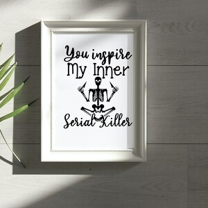 May include: White framed print with black text that reads "You inspire my inner Serial Killer" and a black skeleton illustration sitting in a yoga pose with its middle fingers raised.