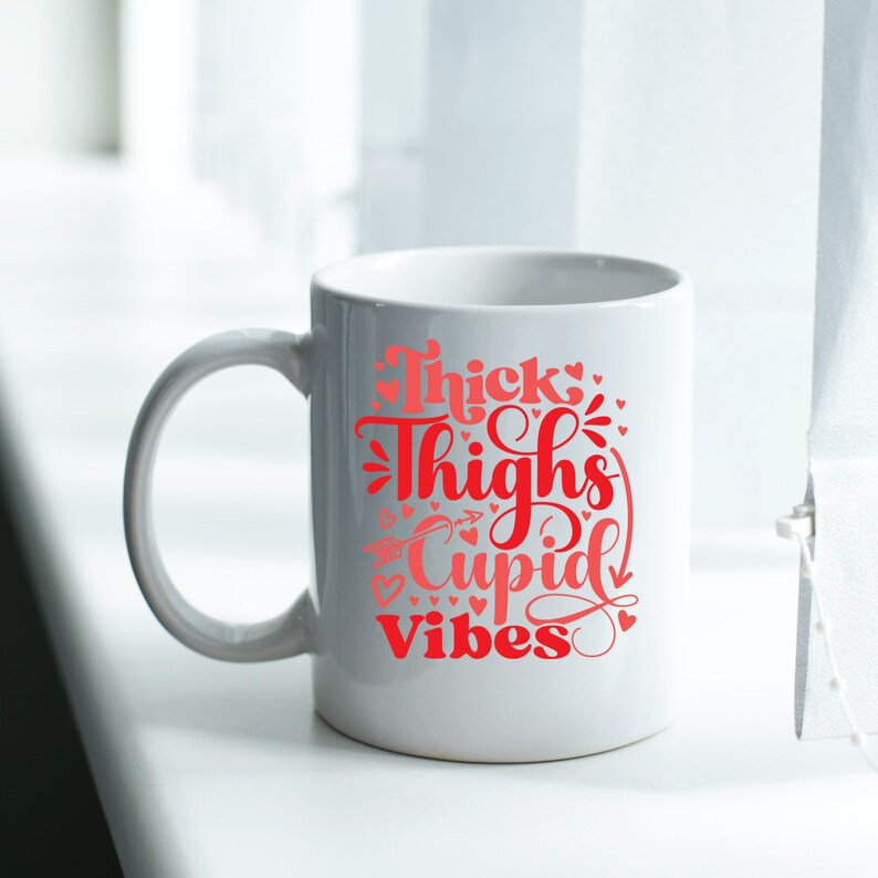May include: White ceramic mug with a red and pink graphic that says "Thick Thighs Cupid Vibes" with small hearts around the text.