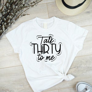 May include: White t-shirt with black text that reads "Talk Thirty to Me".