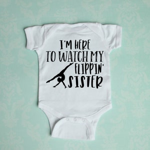 May include: White baby onesie with black text that reads "I'm here to watch my flippin' sister". A black silhouette of a gymnast is shown performing a back handspring.
