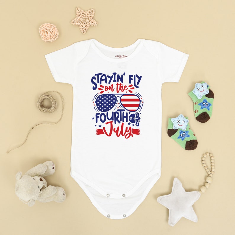 May include: White baby onesie with a red, white, and blue graphic that says "Stayin' Fly on the Fourth of July" with sunglasses that have the American flag on them.