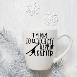 May include: White ceramic mug with a black silhouette of a gymnast and the text "I'm here to watch my flippin' sister".
