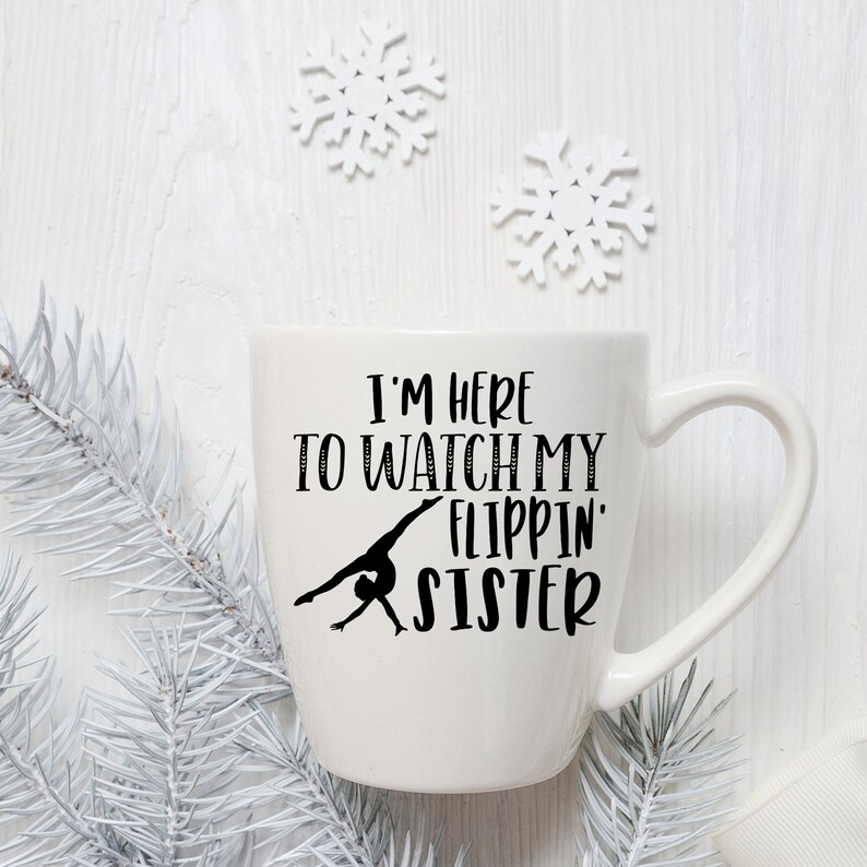 May include: White ceramic mug with a black silhouette of a gymnast and the text "I'm here to watch my flippin' sister".