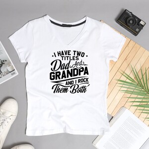 May include: White V-neck t-shirt with black text that reads "I have two titles Dad and Grandpa and I rock them both".