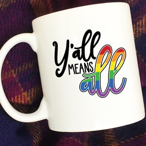 May include: White ceramic coffee mug with a black and rainbow design that says "Y'all means all".