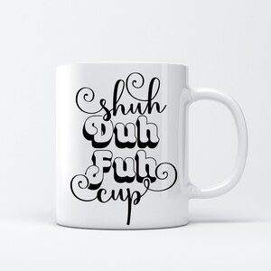 May include: White ceramic mug with the phrase "Shuh Duh Fuh Cup" in black, stylized lettering. The mug has a curved handle and a simple, clean design, suitable for coffee or tea.