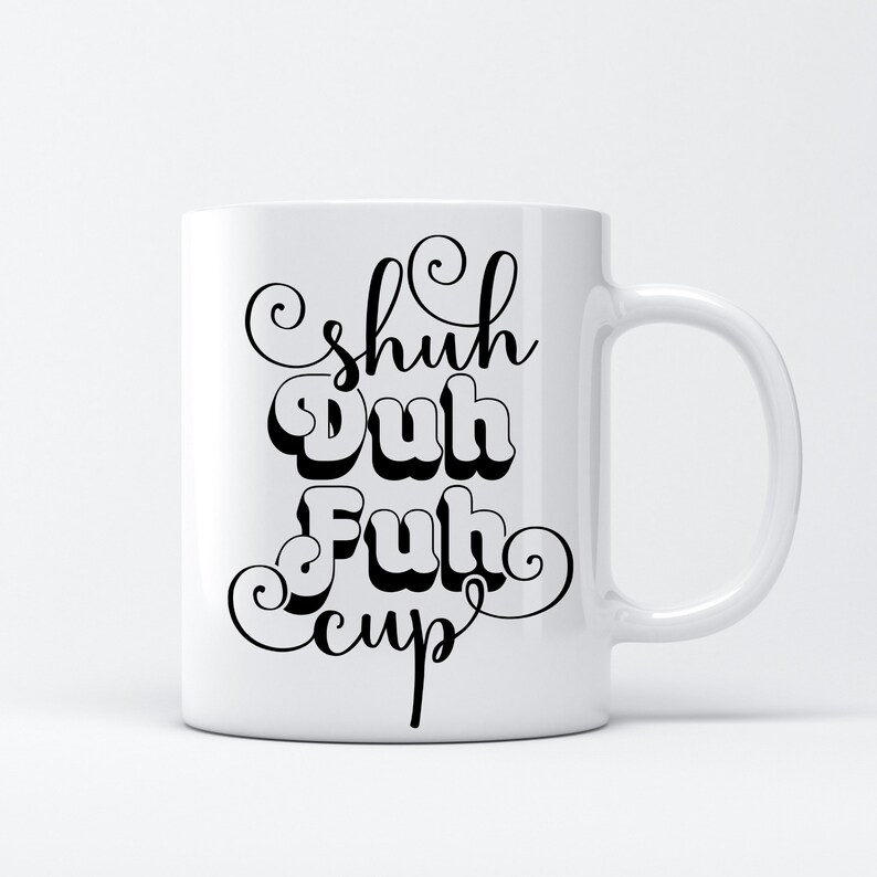 May include: White ceramic mug with the phrase "Shuh Duh Fuh Cup" in black, stylized lettering. The mug has a curved handle and a simple, clean design, suitable for coffee or tea.