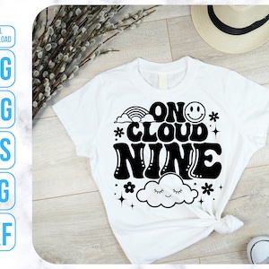 May include: White t-shirt with black text that reads "On Cloud Nine" in a retro font. The text is surrounded by a cloud, stars, and a rainbow.