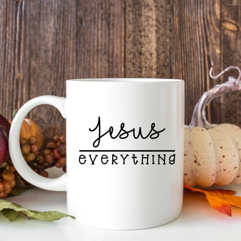 K&ouml;nnte beinhalten: Wei&szlig;e Keramik-Kaffeetasse mit schwarzem Text, der "Jesus Everything" lautet. Die Tasse steht auf einer Holzoberfl&auml;che mit Herbstlaub.