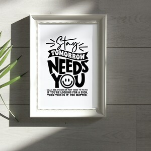 May include: Black and white typography print with the text "Stay Tomorrow Needs You" and a smiley face. The print also includes the text "Call 1-800-273-8255 or text HOME to 741741. If you're looking for a sign, then this is it. You matter."