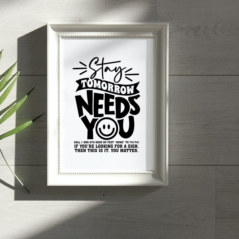 May include: Black and white typography print with the text "Stay Tomorrow Needs You" and a smiley face. The print also includes the text "Call 1-800-273-8255 or text HOME to 741741. If you're looking for a sign, then this is it. You matter."