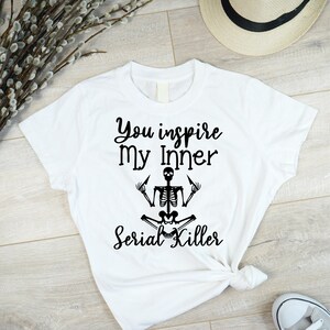 May include: White t-shirt with black text that reads "You inspire my inner Serial Killer" and a black skeleton illustration in a yoga pose.