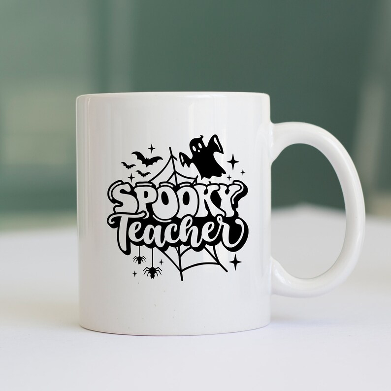 Pu&ograve; includere: Una tazza da caff&egrave; in ceramica bianca con un design nero di un fantasma, ragnatele, pipistrelli e il testo "Spooky Teacher".