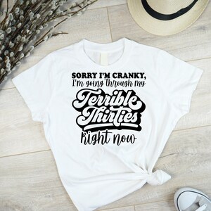 May include: White t-shirt with black text that reads "Sorry I'm Cranky, I'm going through my Terrible Thirties Right Now".