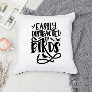 Puede incluir: Coj&iacute;n blanco con texto negro que dice "Easily Distracted by Birds". El texto est&aacute; en una fuente decorativa e incluye un dise&ntilde;o de p&aacute;jaros.