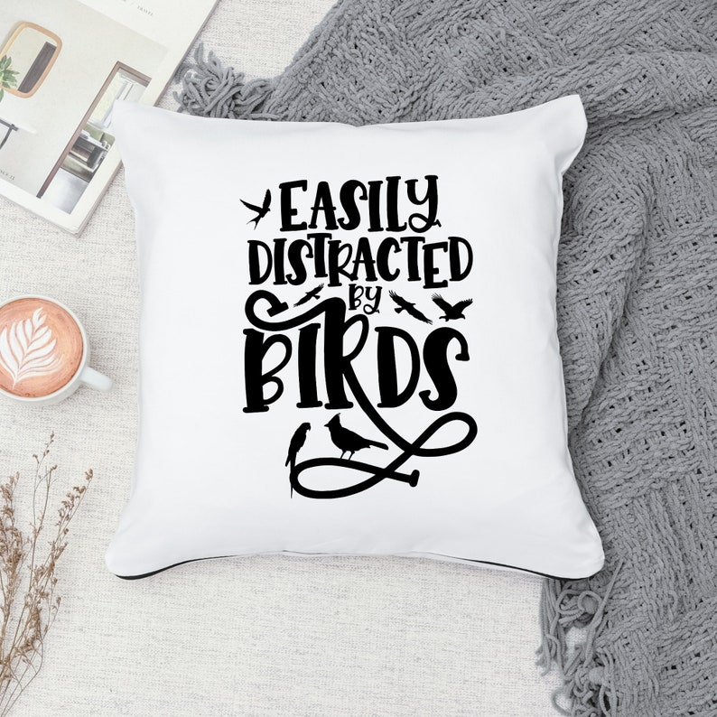 Puede incluir: Coj&iacute;n blanco con texto negro que dice "Easily Distracted by Birds". El texto est&aacute; en una fuente decorativa e incluye un dise&ntilde;o de p&aacute;jaros.
